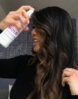 Photo of model with curly brown hair spraying her hair with HOLD Volumizing Hair Spray-InStyler